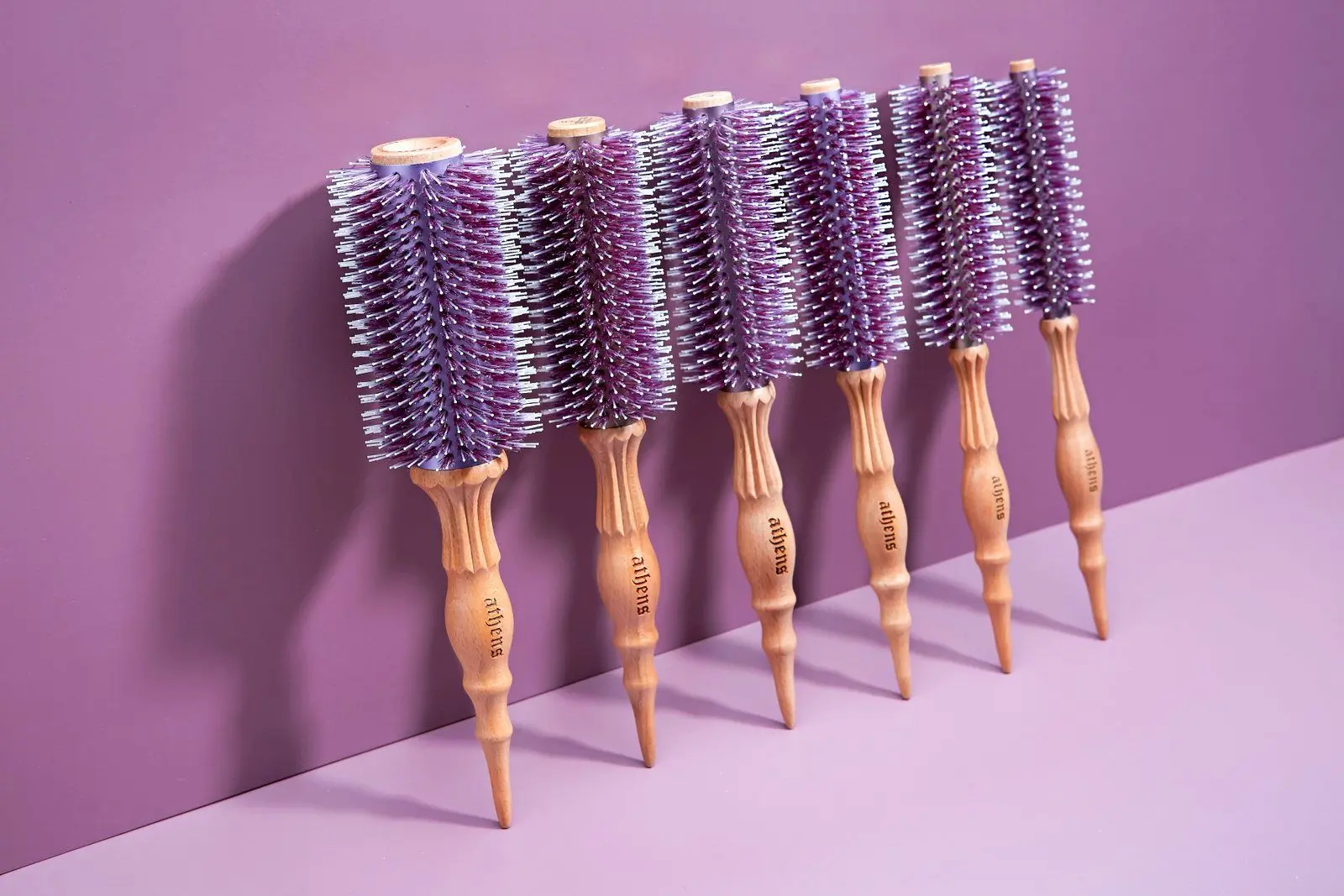 A row of Athens Goddess Roll Brushes in graduated sizes leaning against a violet wall