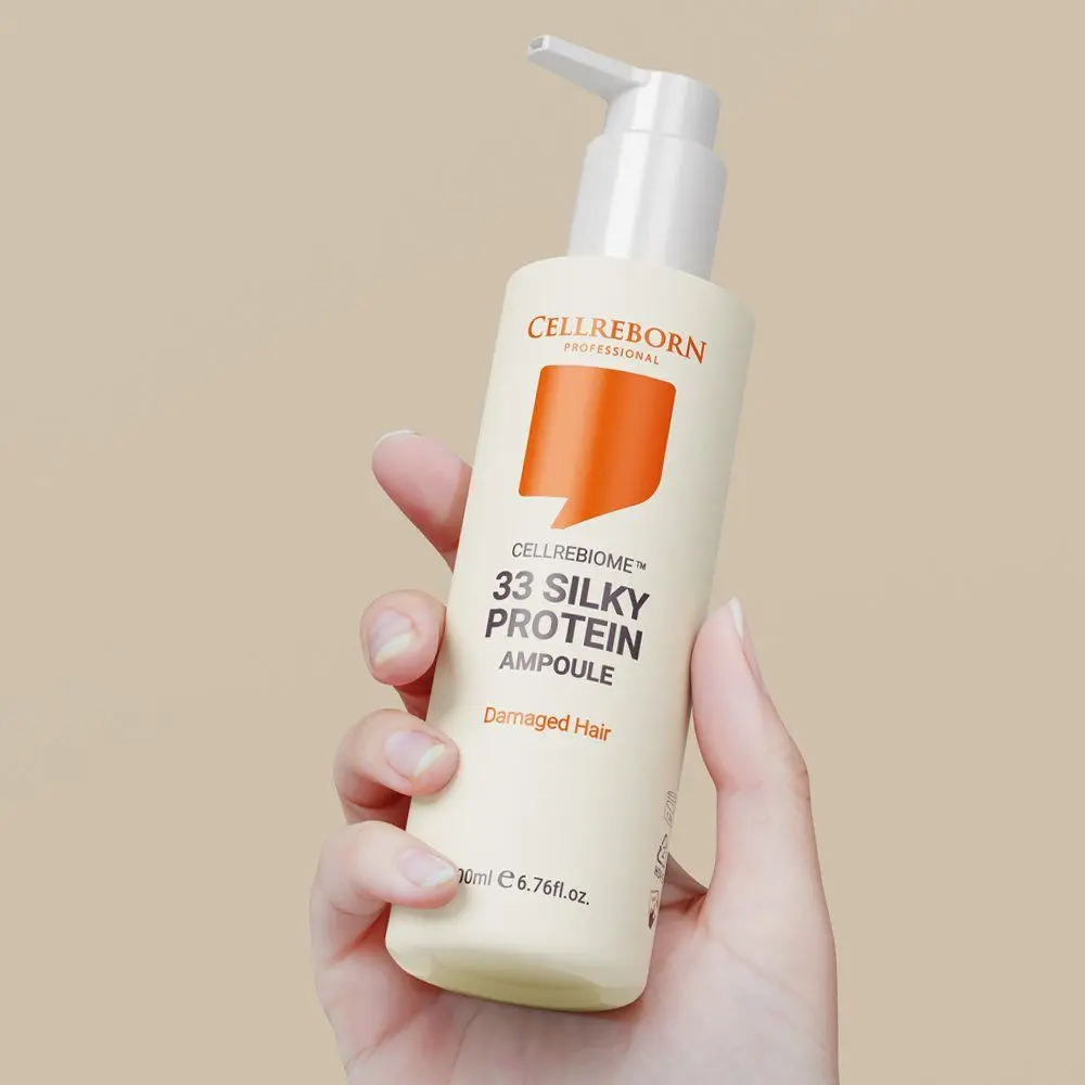 A hand holding a Cellrebiome 33 Silky Protein Ampoule bottle against a beige backdrop