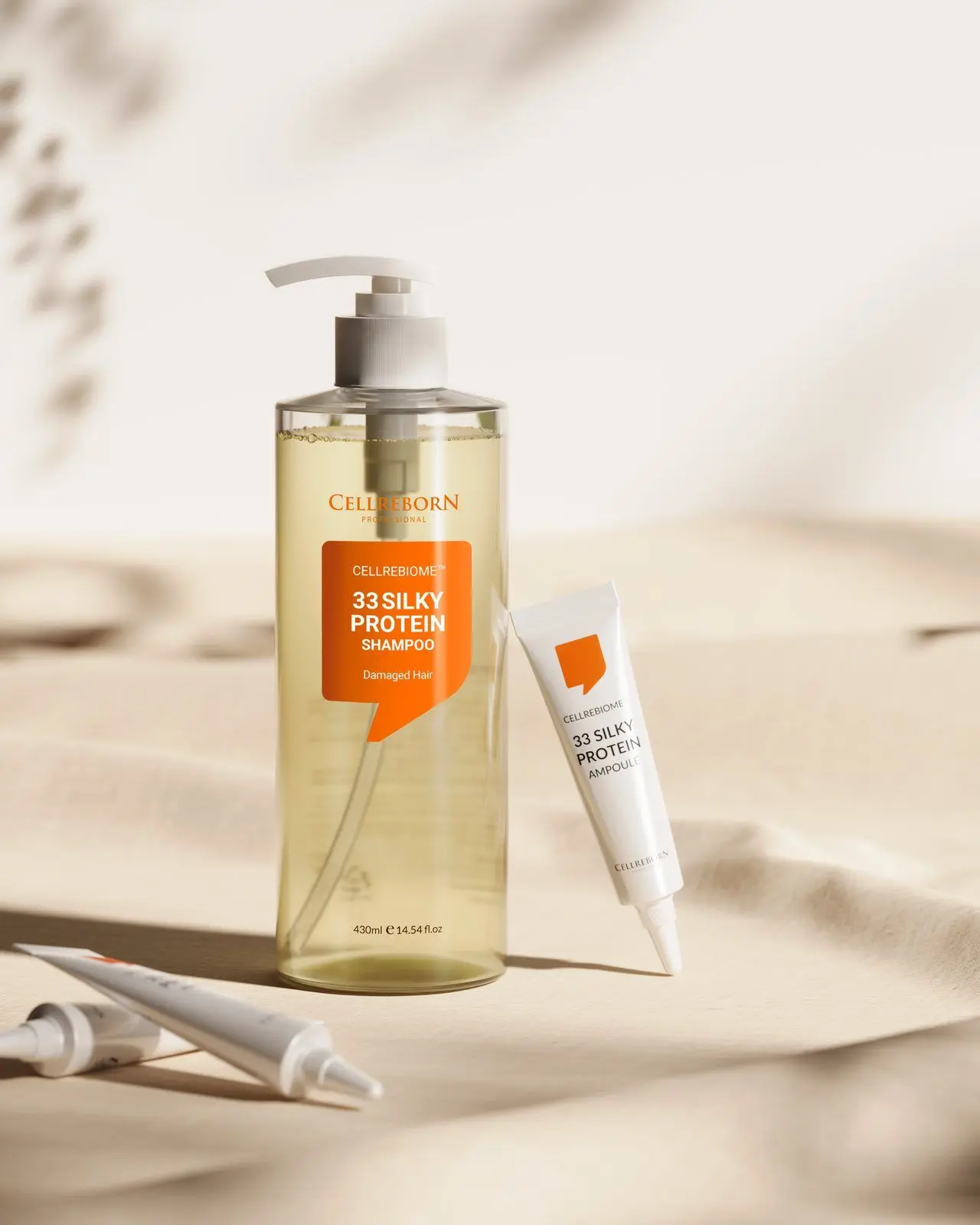 Cellrebiome 33 Silky Protein Shampoo bottle on pale sand with a small tube beside it and soft leaf shadows