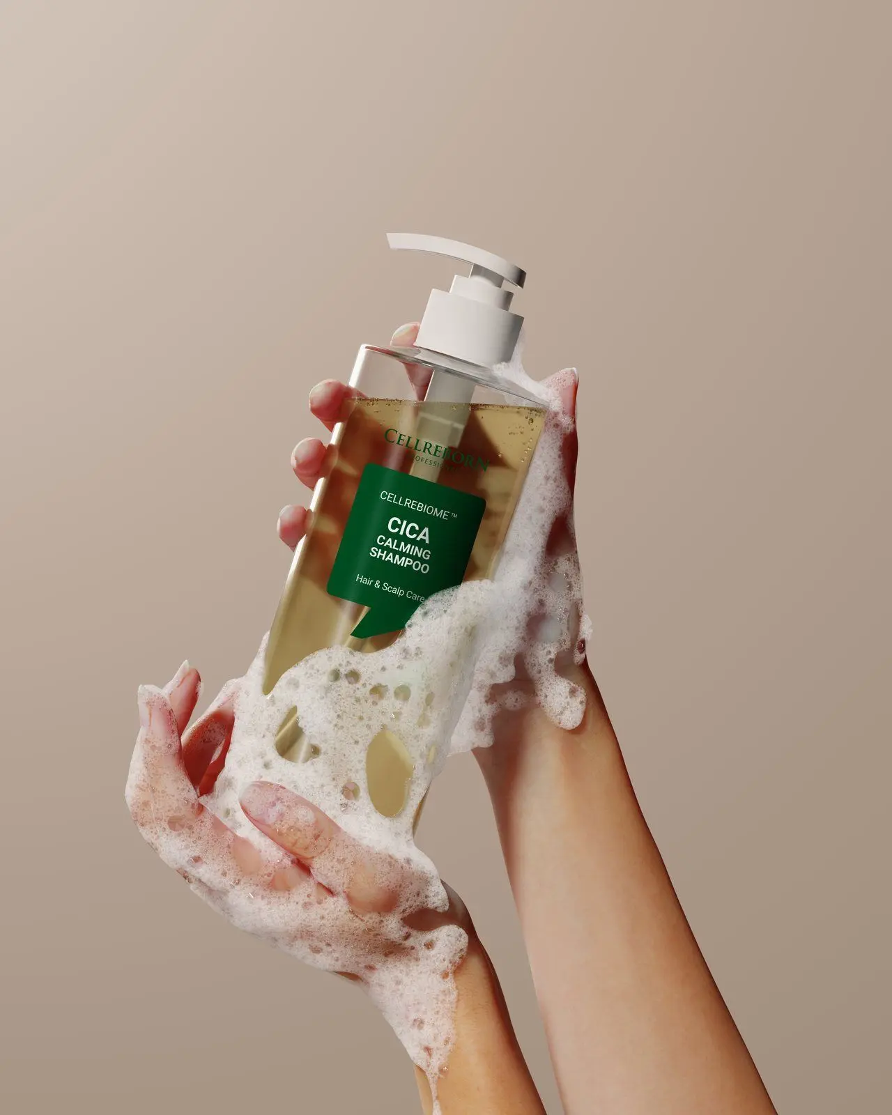 Hands with white lather holding a Cellrebiome Cica Calming Shampoo bottle against a warm beige backdrop