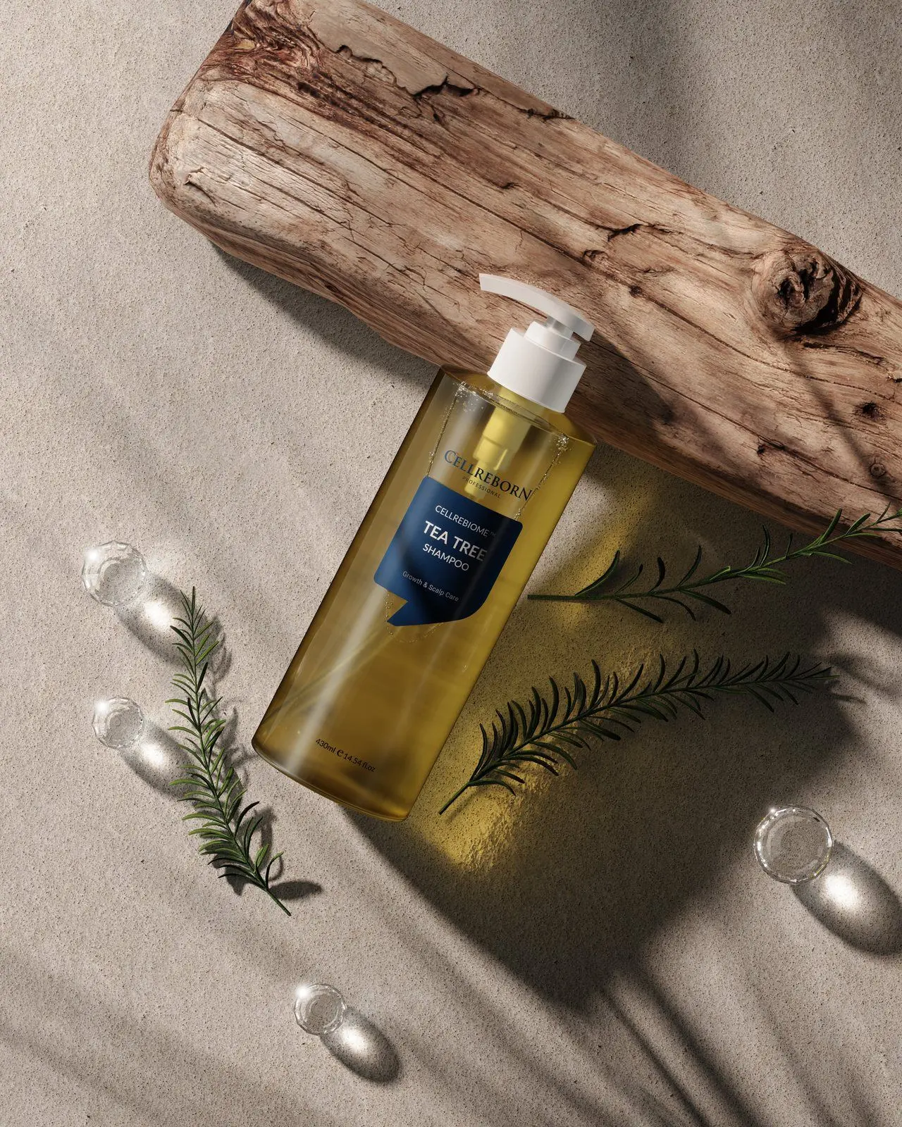 Cellrebiome Tea Tree Shampoo bottle on sand beside driftwood and rosemary, seen from above